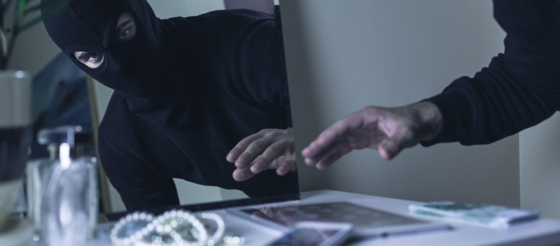 Unbekannter Hacker greift Computer mit dunkler Maske und dunklem Pullover an.