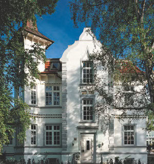 Hochwertiges historisches Gebäude mit weißen Fassaden und großen Fenstern in einer grünen Umgebung.