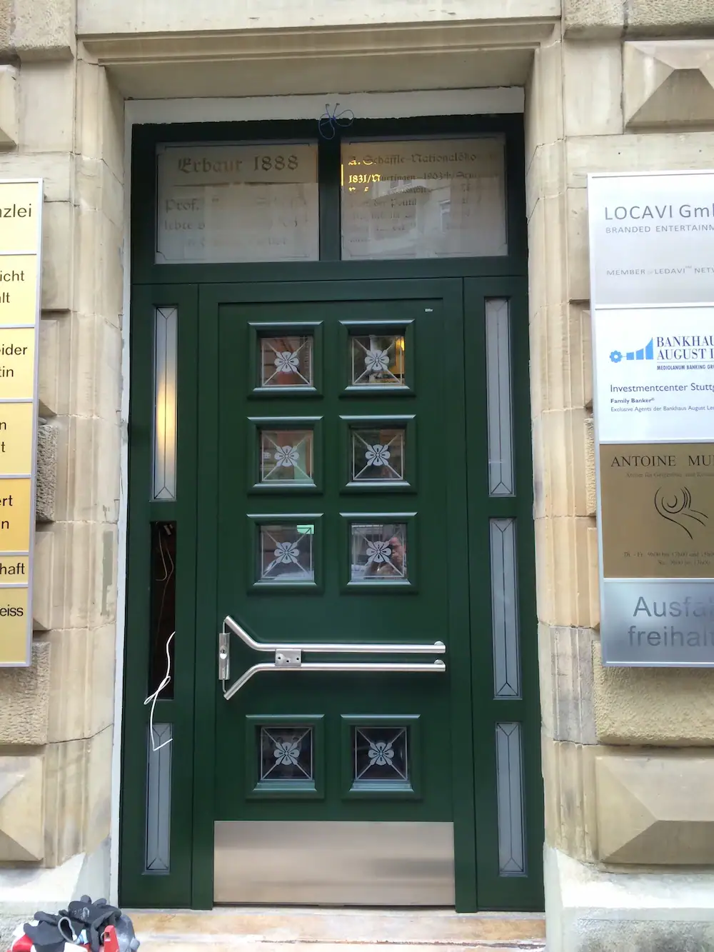 Alte grüne Haustür mit dekorativem Schließmechanismus und Fenstern, Blickfang für Immobilien und Gebäudereparatur.